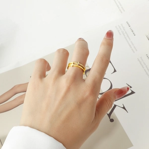 Detail eines doppellagigen goldenen Kreuzrings mit Strasssteinen an der Hand