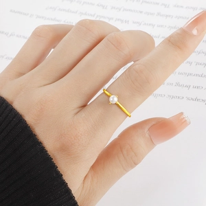 Eleganter Gold-Titanstahlring mit weißer Perle auf Handmodell über Buchhintergrund