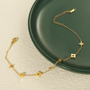 Detail der goldenen Titanstahl-Fußkette mit Kleeblatt- und Sternanhängern auf Keramik