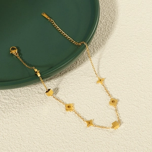 Goldenes Titanstahl-Fußkettchen mit Kleeblatt-Anhängern auf einem eleganten dunklen Teller