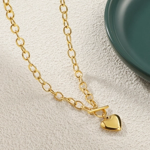 Detail of gold heart pendant necklace featuring heavy chain links and stylish OT clasp