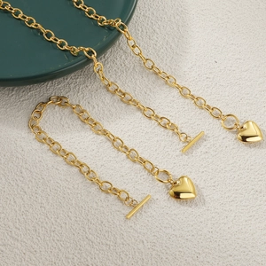 Gold chain necklace with heart pendant and toggle clasp on a dark green ceramic plate