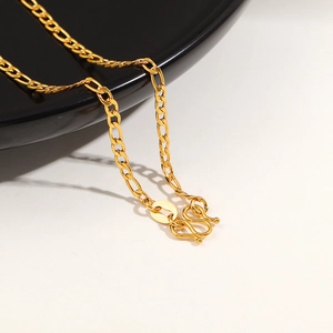 Macro shot of 24K gold plated Figaro chain necklace showing detailed M-clasp and texture