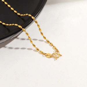 Macro detail of 24K gold-plated oval bead chain with traditional M-shaped clasp closure