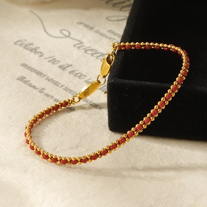 Detail of red braided rope bracelet with gold beads and 'K' engraved metal charm