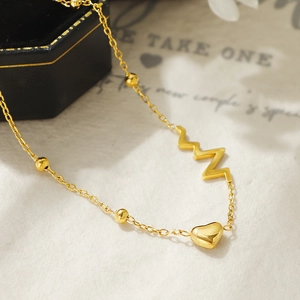 Detalle macro de tobillera de titanio dorado con diseño de corazón y latido