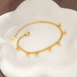 Detail of gold bean tassel bracelet with lobster clasp and adjustable chain on ceramic plate