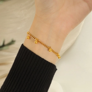 Close-up of a delicate gold beaded tassel bracelet worn on a wrist with black knitwear