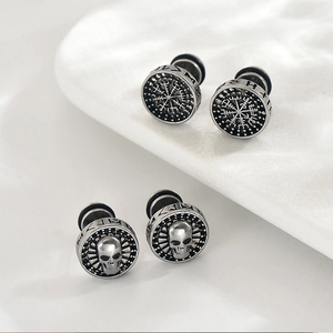 Detailed close-up of retro silver skull and Viking compass stud earrings with rune carvings