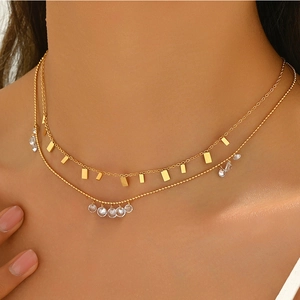 Gros plan d'un collier double épaisseur doré avec pendentif carré et charmes en cristal