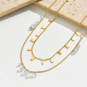 Détail d'un collier doré multicouche avec plaques géométriques et cristaux clairs