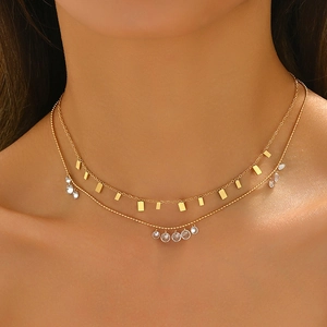 Détail d'un collier doré à deux rangs avec mini breloques carrées et perles de cristal