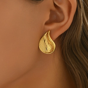 Pendientes dorados de gota con textura en relieve usados en la oreja en ángulo de 45 grados