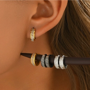 Detalle macro de pendientes en C con patrón griego clásico en metal dorado y negro