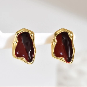 Dettaglio macro di orecchini irregolari placcati in oro con smalto rosso intenso