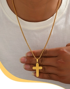 Close-up of a golden vintage cross pendant necklace worn with a classic box chain