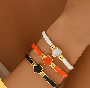 Détail de trois bracelets trèfle en noir, blanc et orange avec dorure et cristaux brillants