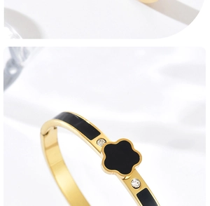 Détail d'un bracelet en acier doré avec trèfle en émail noir et cristaux de zircon brillants