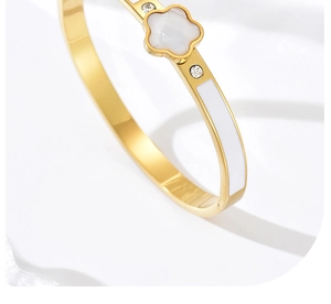 Détail macro du bracelet trèfle doré avec émail blanc et incrustations de zircon