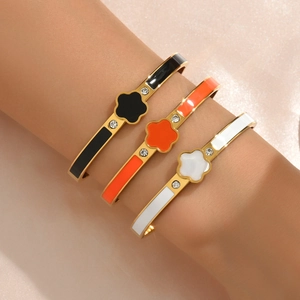 Bracelets trèfle dorés avec finition émail noir, orange et blanc portés par un mannequin