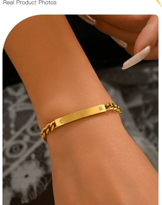 Detail of gold-plated Cuban chain bracelet with rectangular ID plate and two white crystals