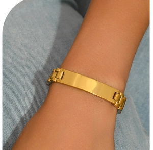 Close-up of golden stainless steel strap bracelet with polished rectangular plate on denim