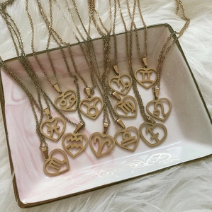 Gold plated stainless steel heart necklaces with twelve zodiac signs on marble tray