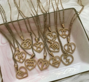 Flat lay of twelve gold zodiac heart necklaces on a marble tray and plush background