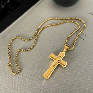 Detail of gold double-layered cross pendant with box chain and lobster clasp on grey texture