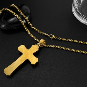 Detail of golden cross pendant with brushed finish and rugged box chain on a black stone