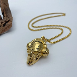 Detail eines goldenen Totenkopf-Anhängers mit Kopfhörern an einer goldenen Box-Kette