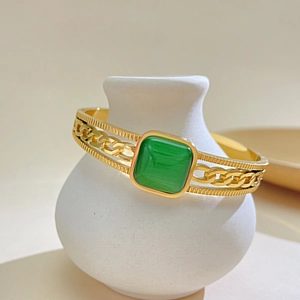 Detailed macro of gold-plated open cuff bracelet with hollow chain links and green cat-eye stone
