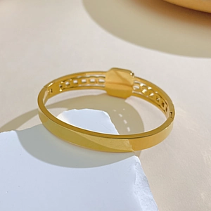 Polished gold stainless steel hollow geometric bangle on a white stone background