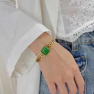 Detail of vintage gold-plated cutout cuff bracelet with a green square gemstone