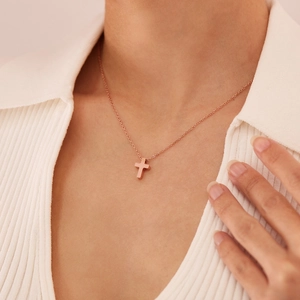 Vue rapprochée du collier croix en or rose porté par un mannequin sur un haut blanc