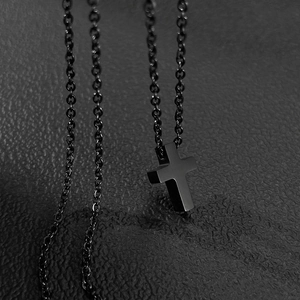 Gros plan sur un collier pendentif croix noir minimaliste avec finition mate brossée