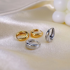 Gros plan de boucles d'oreilles huggies épaisses or et argent sur soie beige