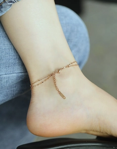 Detail of rose gold double-layered heart anklet with beads on female model foot