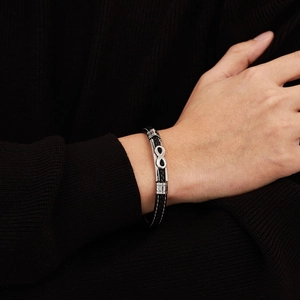 Detail of infinity symbol charm on black braided leather bracelet worn on wrist