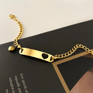 Macro shot of gold stainless steel bracelet with heart cutout ID plate and heart charm