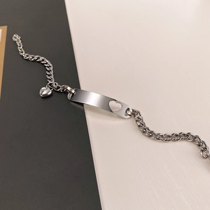 Close-up of polished stainless steel bracelet featuring heart cutout bar and small charm