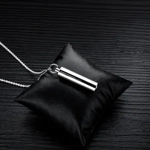 Macro shot of polished stainless steel cylinder pendant for ashes on black leather cushion