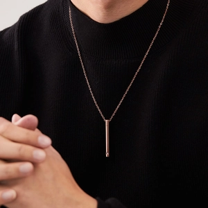 Détail d'un collier avec pendentif cylindre en or rose porté sur un pull en maille noir