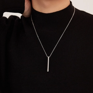 Collier urne minimaliste en argent avec pendentif cylindre porté sur un pull à col roulé noir