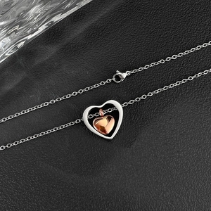 Dettaglio di un ciondolo a cuore bicolore con strati argento e oro rosa su pelle nera