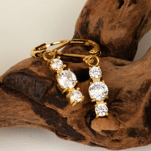 Elegant gold earrings with three graduated round zircons on dark wood background