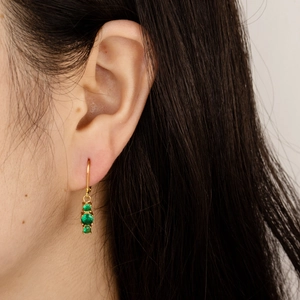 Macro shot of gold drop earrings with three vertical round green emerald-style gemstones