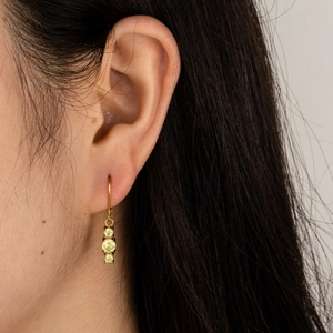 Detailed close-up of a gold earring with three yellow round zircons worn by a model