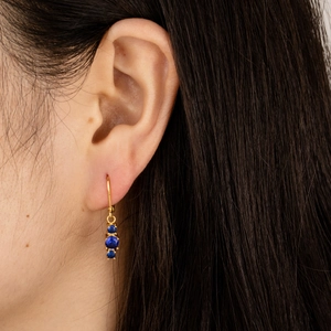 Close-up of gold drop earrings with three round blue cubic zirconia on model