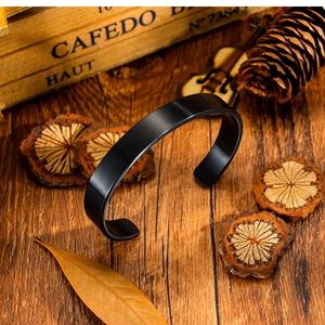 Detalle de una pulsera rígida negra mate sobre un fondo de madera rústica con accesorios